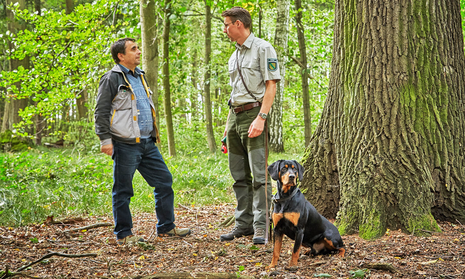 Förster mit Hund im Gespräch mit einem Waldbesitzer im Wald